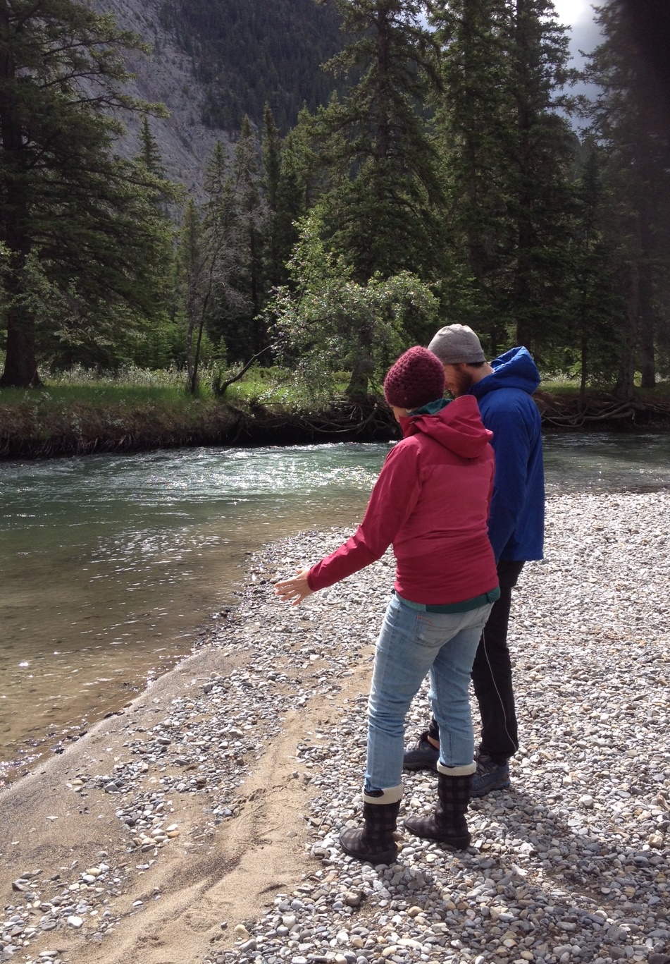 two people standing near riverbank in the mountains